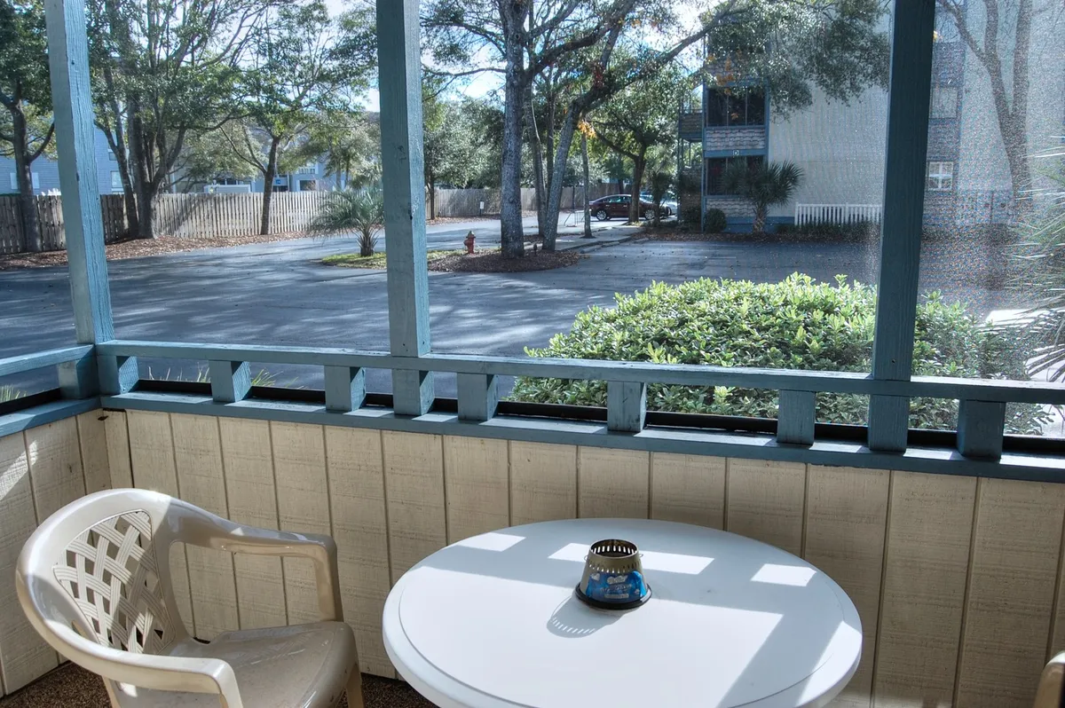 A calm screened-in porch scene with a round table, a plastic chair, and a decorative centerpiece. The enclosed design and tranquil setup create an inviting spot for morning coffee, reading, and quiet conversations, echoing the serene mood described in the section.