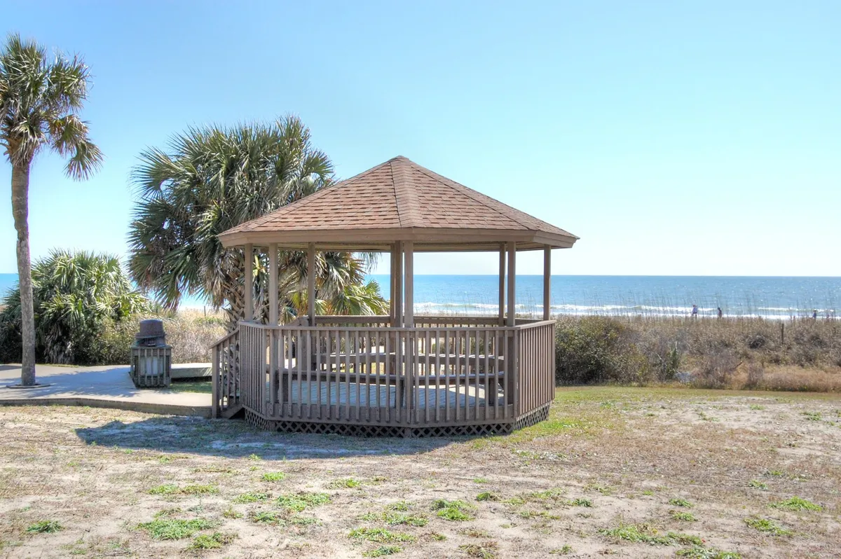 A serene scene with a wooden gazebo overlooking the ocean, surrounded by palm trees. The setting invites gatherings with friends, sunset watching, or quiet moments after a night out, embodying both relaxation and social potential.