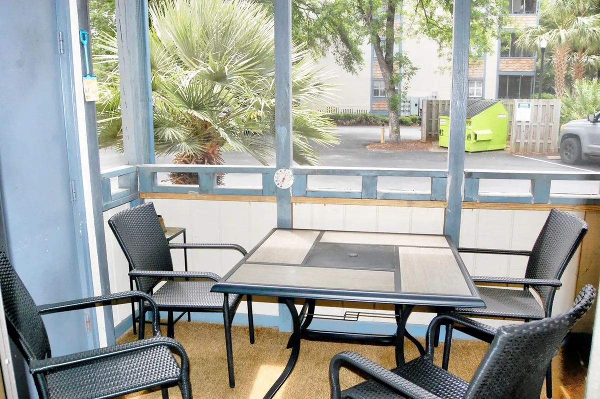 This image features a screened-in porch with a table and chairs, looking out toward palm trees through the screen. The natural light, greenery, and relaxed seating evoke a breezy atmosphere ideal for enjoying meals, reading, or socializing while feeling connected to the outdoors.